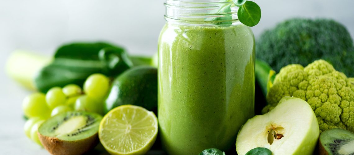 Glass jar mugs with green health smoothie, kale leaves, lime, apple, kiwi, grapes, banana, avocado, lettuce. Copy space. Raw, vegan, vegetarian, alkaline food concept. Banner.